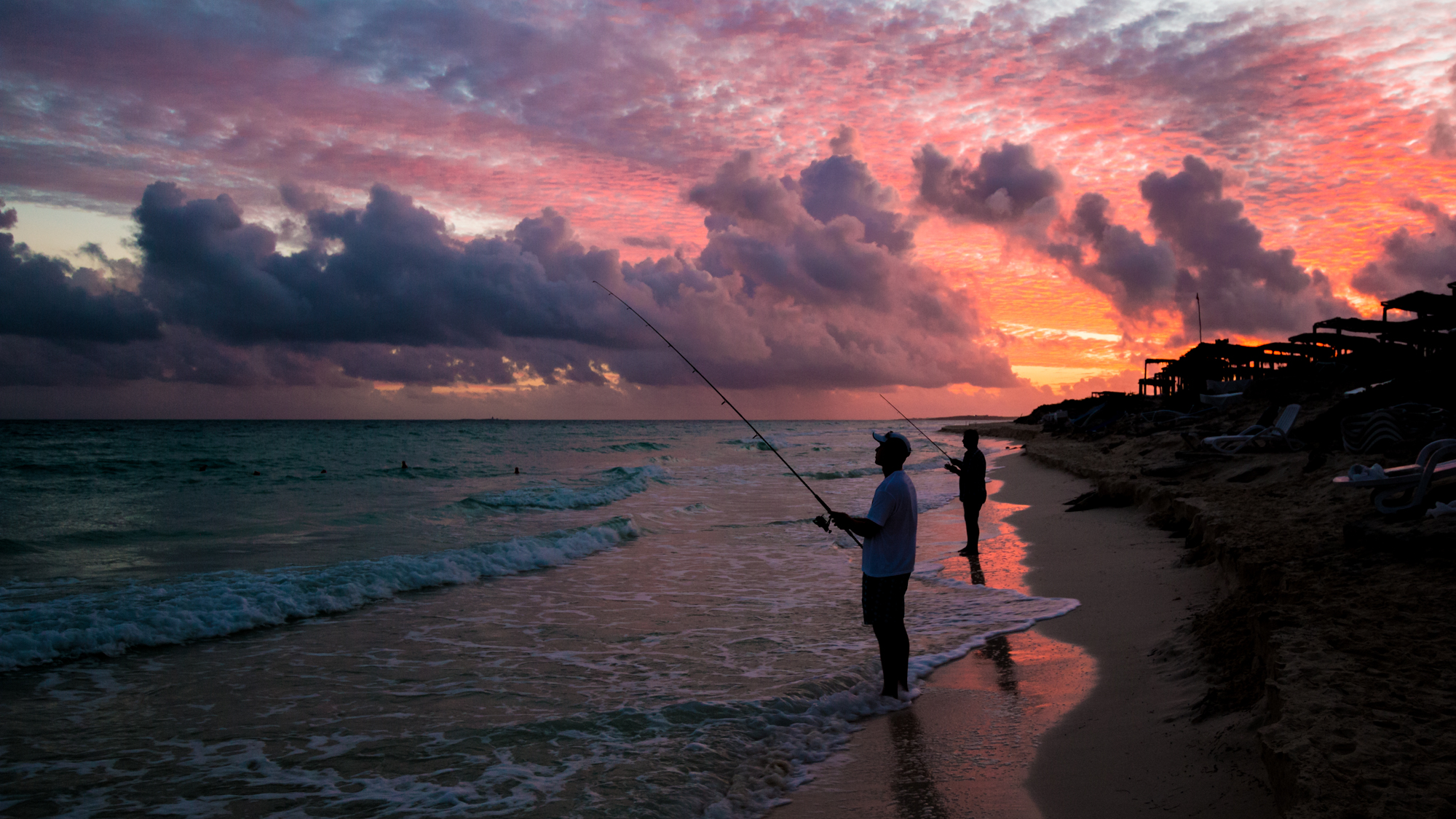 Silhouettes de pêcheurs avec un ciel rose orangé sur la plage